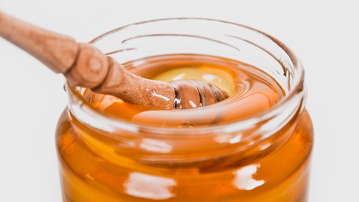 蜂蜜玻璃罐与木质蜂蜜勺的静物照片